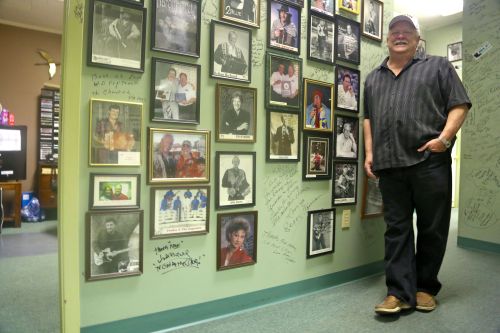 Paul Marx, owner of KBON radio station in Eunice, LA, stands near a collection of autographed photos and a wall covered in signatures. His station mostly plays music by Louisiana musicians, including Jamie Bergeron & The Kickin’ Cajuns, whose song “Registered Coonass,” has not been received well by all Louisianans. (Photo: Veronica Zaragovia)